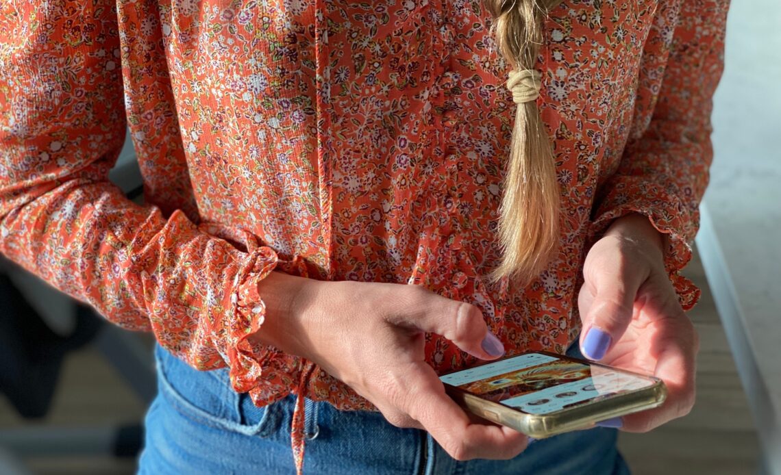 A stylish millennial woman with a long braid is using her mobile device to check her social media