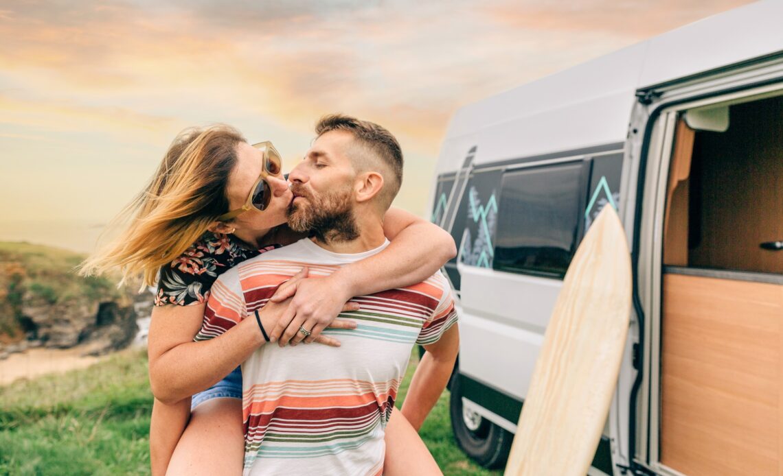 Couple kissing piggybacking next to their camper van during a trip