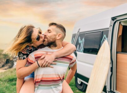 Couple kissing piggybacking next to their camper van during a trip